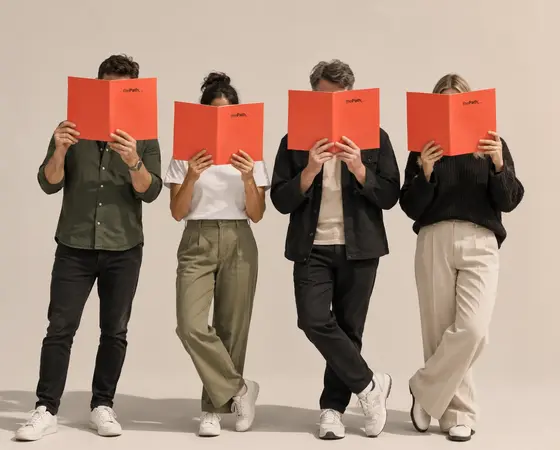 Four people standing in a row, each reading the same slim red booklet.